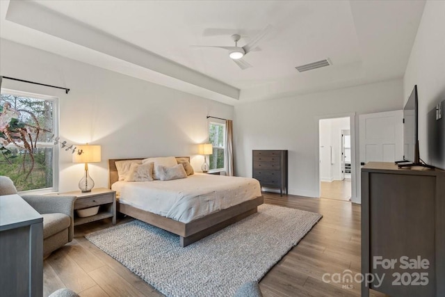 bedroom with visible vents, a raised ceiling, a ceiling fan, and wood finished floors