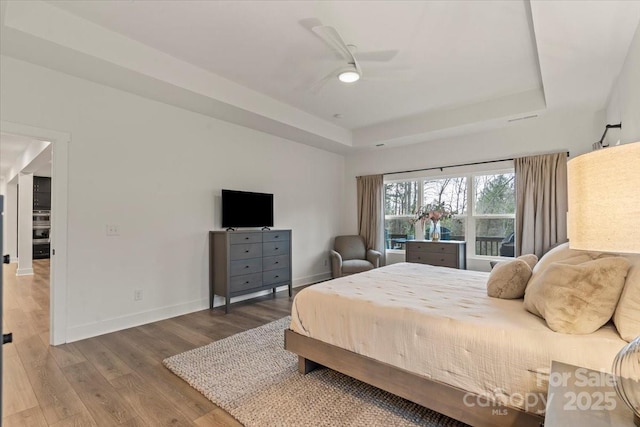 bedroom featuring ceiling fan, baseboards, a tray ceiling, and wood finished floors