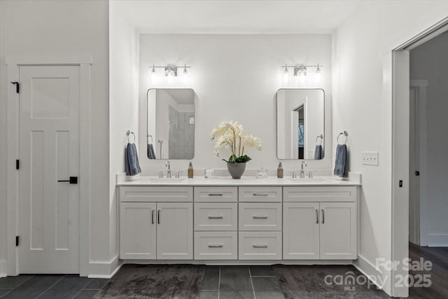 bathroom featuring double vanity, tiled shower, baseboards, and a sink