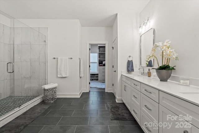 bathroom with baseboards, double vanity, a stall shower, a sink, and tile patterned floors