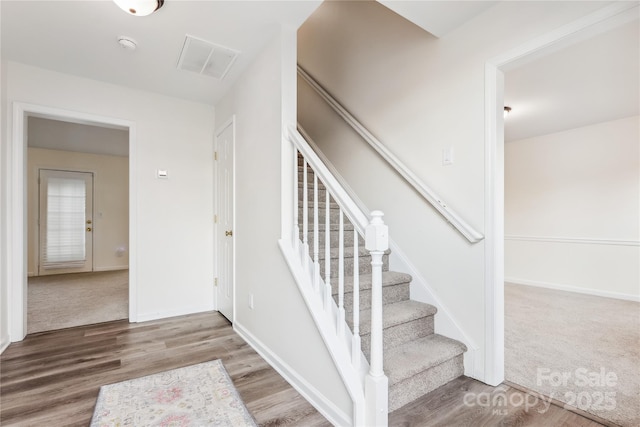 stairs featuring carpet flooring, wood finished floors, visible vents, and baseboards