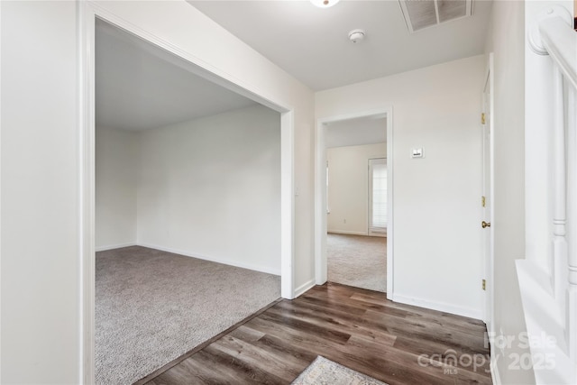 spare room with dark colored carpet, visible vents, baseboards, and dark wood-style flooring