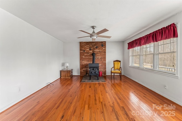 interior space with baseboards, a wood stove, ceiling fan, and wood-type flooring