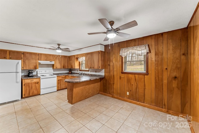 kitchen featuring white appliances, a peninsula, under cabinet range hood, dark countertops, and brown cabinets