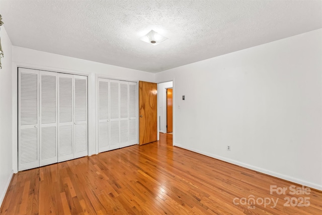 unfurnished bedroom with baseboards, two closets, hardwood / wood-style floors, and a textured ceiling