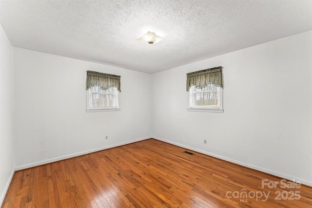 spare room featuring a healthy amount of sunlight, baseboards, and hardwood / wood-style flooring