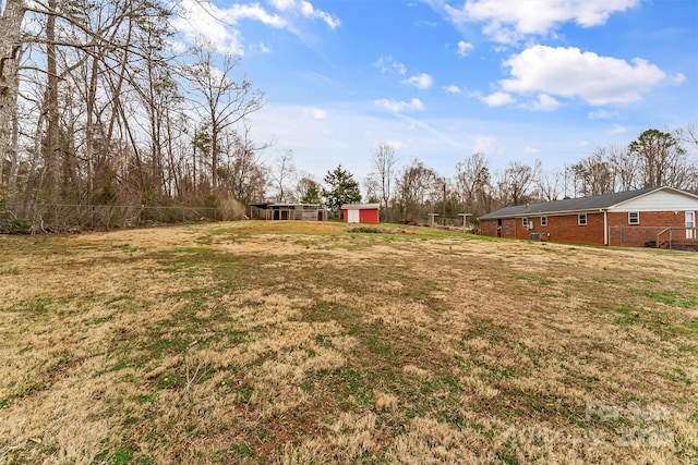 view of yard featuring a storage shed, an outdoor structure, driveway, and fence