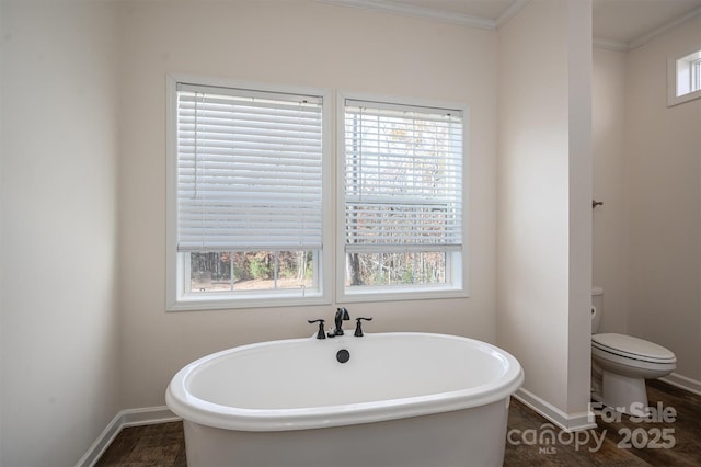 bathroom with baseboards, a soaking tub, toilet, and crown molding