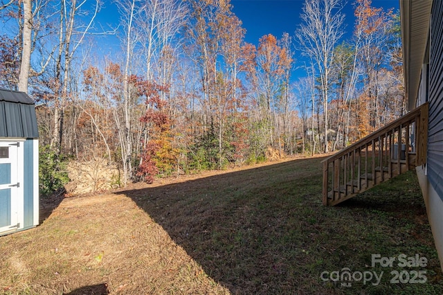 view of yard featuring a forest view, stairs, a storage shed, and an outdoor structure