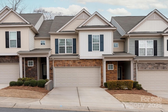 view of front of property with board and batten siding, an attached garage, stone siding, and driveway