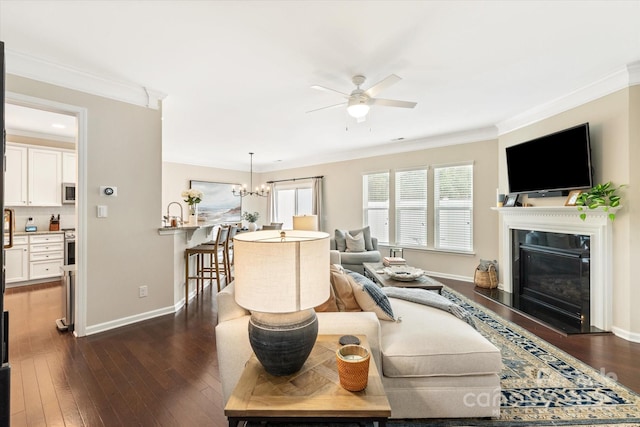 living area featuring a glass covered fireplace, crown molding, dark wood-style floors, and ceiling fan with notable chandelier