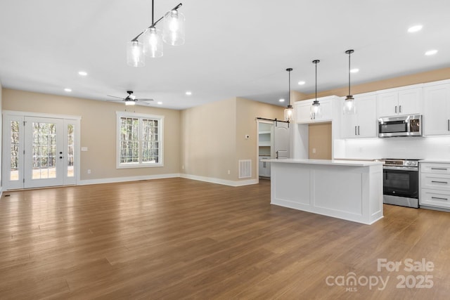 kitchen with visible vents, a kitchen island, appliances with stainless steel finishes, white cabinetry, and a barn door