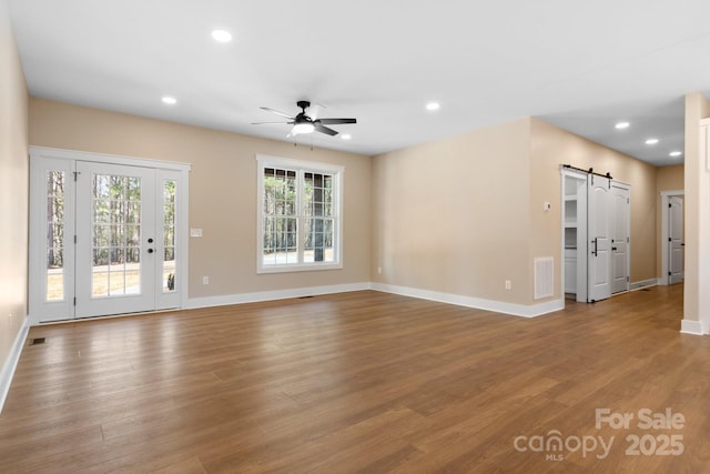 unfurnished living room with visible vents, recessed lighting, a barn door, and wood finished floors