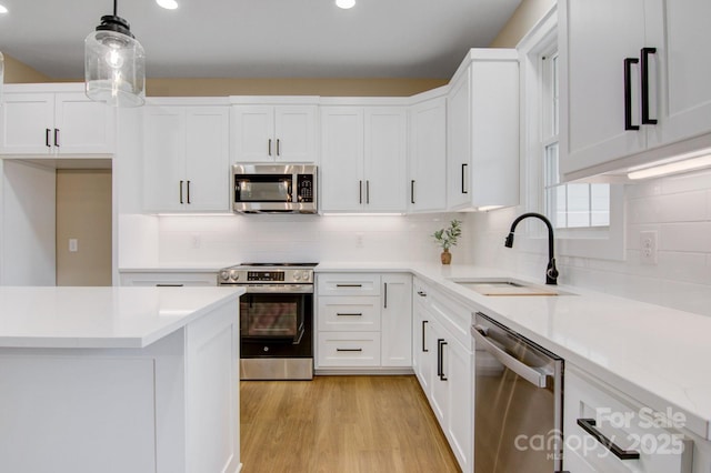 kitchen with a sink, white cabinetry, stainless steel appliances, light wood-style floors, and light countertops