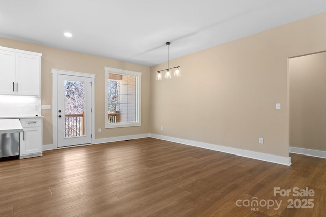 unfurnished dining area featuring recessed lighting, baseboards, an inviting chandelier, and dark wood-style floors