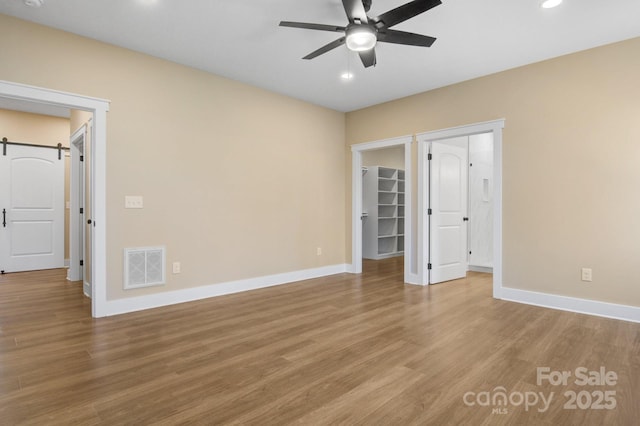 unfurnished bedroom featuring wood finished floors, visible vents, baseboards, a walk in closet, and a barn door