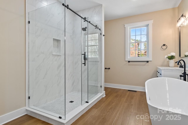 bathroom featuring visible vents, a stall shower, wood finished floors, baseboards, and a freestanding bath