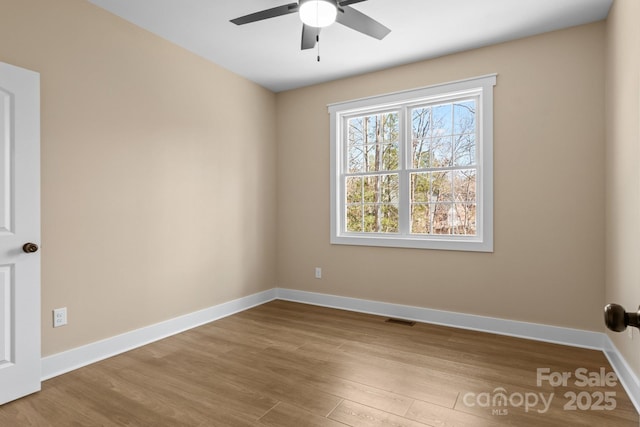 empty room featuring visible vents, a ceiling fan, baseboards, and wood finished floors