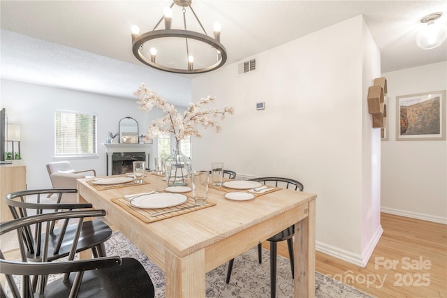 dining area featuring light wood finished floors, baseboards, visible vents, a notable chandelier, and a high end fireplace