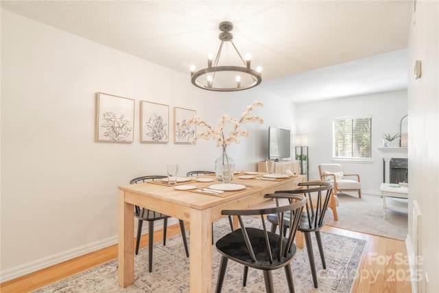 dining space with light wood finished floors, a premium fireplace, a textured ceiling, a chandelier, and baseboards