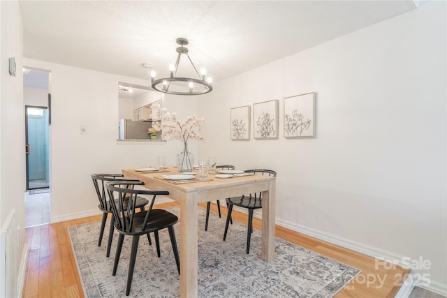 dining space featuring light wood-type flooring, a notable chandelier, and baseboards