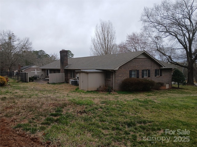 view of home's exterior with a yard, brick siding, central AC unit, and a chimney