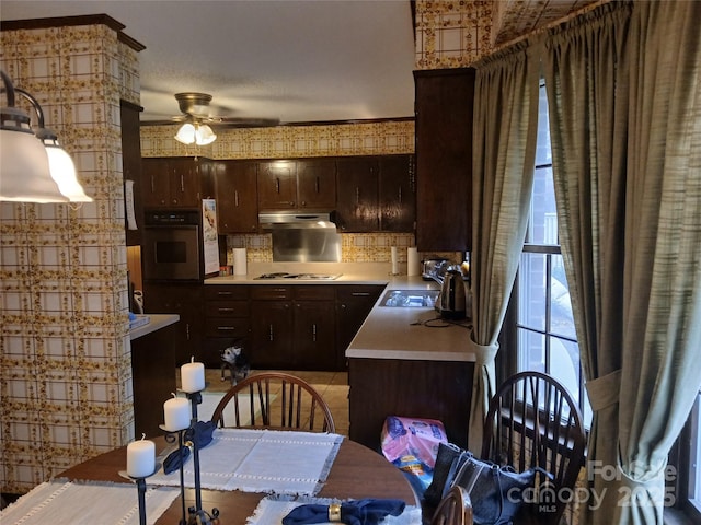 kitchen featuring gas cooktop, a sink, light countertops, under cabinet range hood, and stainless steel oven