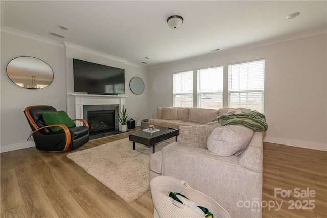 living room featuring baseboards, visible vents, a fireplace with flush hearth, ornamental molding, and wood finished floors