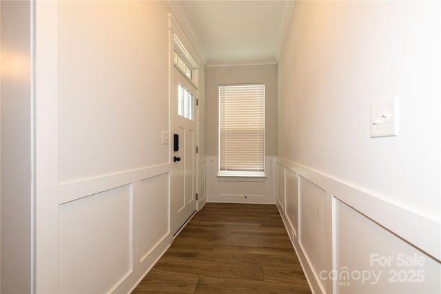 doorway to outside featuring a decorative wall, ornamental molding, dark wood finished floors, and wainscoting