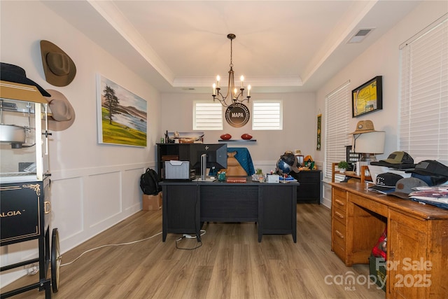 home office with visible vents, a raised ceiling, wainscoting, light wood-type flooring, and a decorative wall