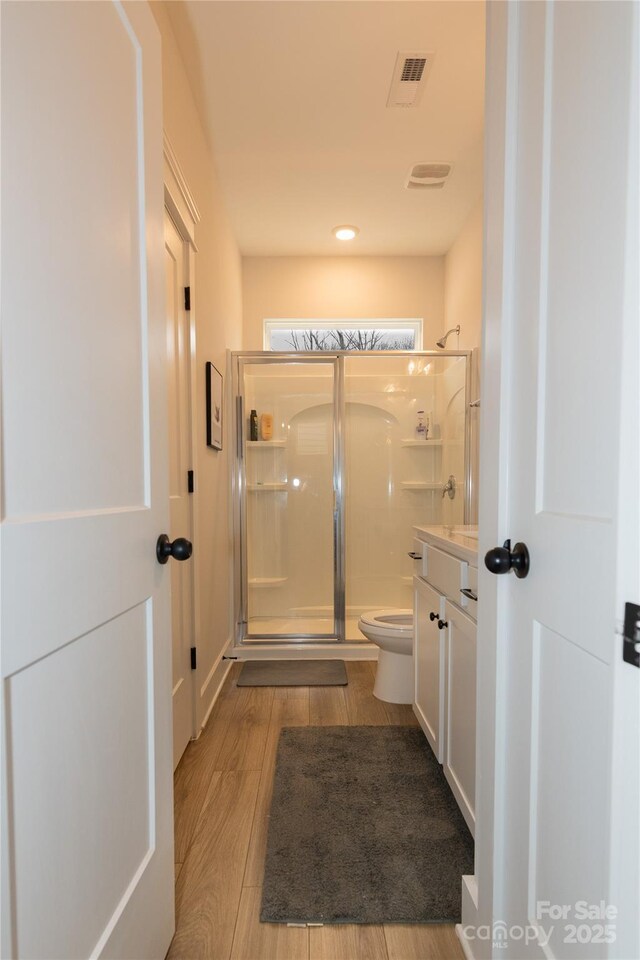 bathroom with visible vents, toilet, wood finished floors, vanity, and a shower stall