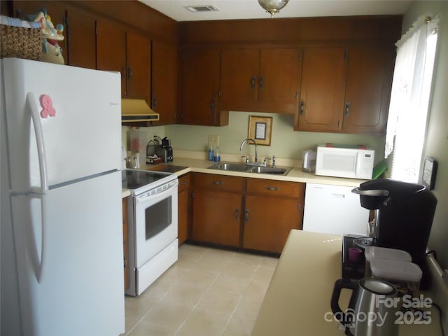 kitchen featuring white appliances, a sink, light countertops, under cabinet range hood, and brown cabinets