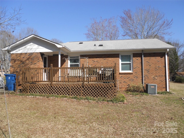 rear view of property with central air condition unit, brick siding, a deck, and a lawn