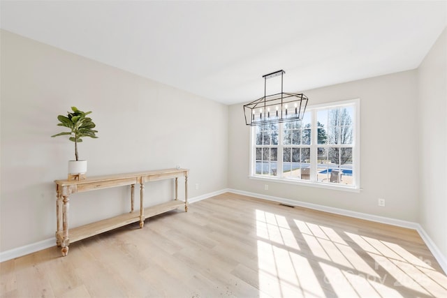 unfurnished dining area featuring visible vents, baseboards, light wood finished floors, and a chandelier