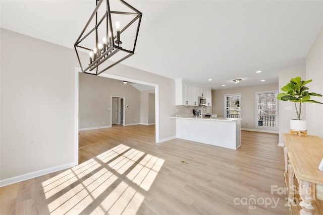 unfurnished living room featuring recessed lighting, a chandelier, baseboards, and light wood-style flooring