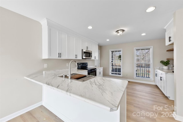 kitchen with stainless steel microwave, light stone countertops, light wood-type flooring, a peninsula, and electric range