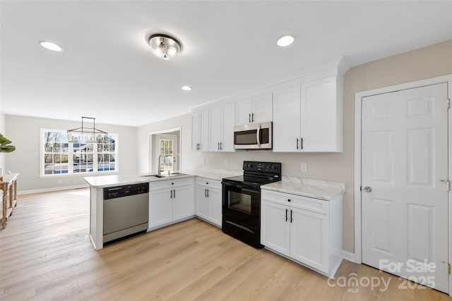 kitchen featuring light wood-type flooring, appliances with stainless steel finishes, a peninsula, white cabinetry, and a sink