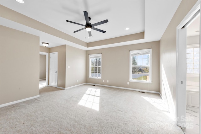 spare room featuring visible vents, baseboards, light colored carpet, a tray ceiling, and a ceiling fan