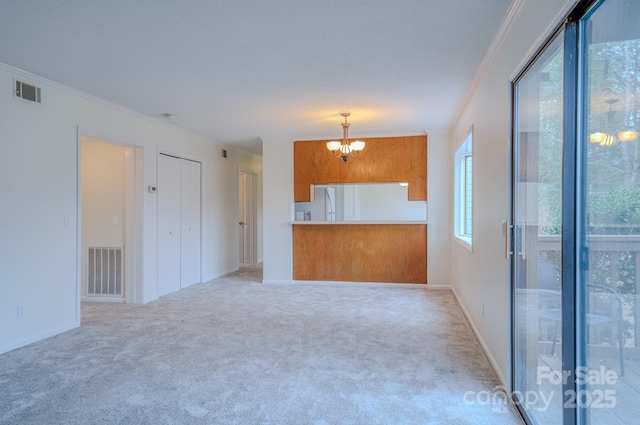 unfurnished living room featuring visible vents, a notable chandelier, ornamental molding, and carpet flooring