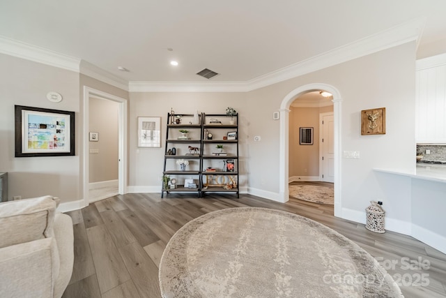 living area with visible vents, crown molding, baseboards, wood finished floors, and arched walkways