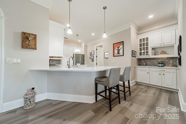 kitchen with a breakfast bar, light countertops, ornamental molding, a peninsula, and white cabinets