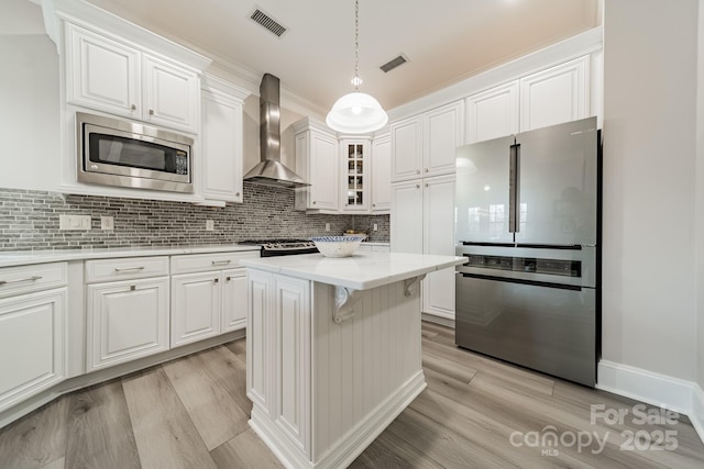 kitchen featuring visible vents, light wood-style flooring, appliances with stainless steel finishes, wall chimney range hood, and tasteful backsplash