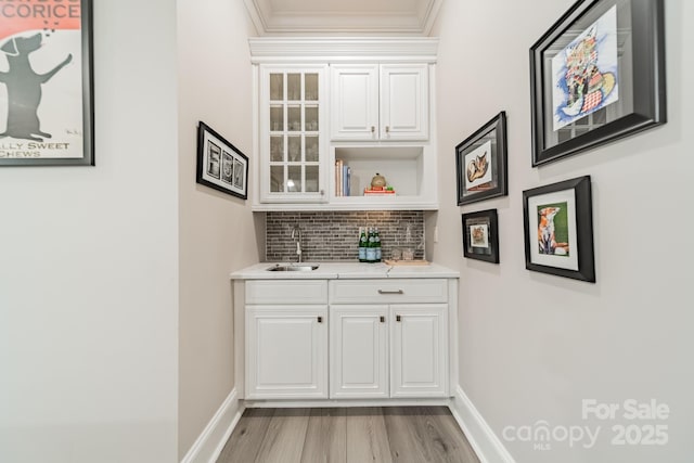 bar featuring backsplash, baseboards, light wood-style flooring, wet bar, and a sink