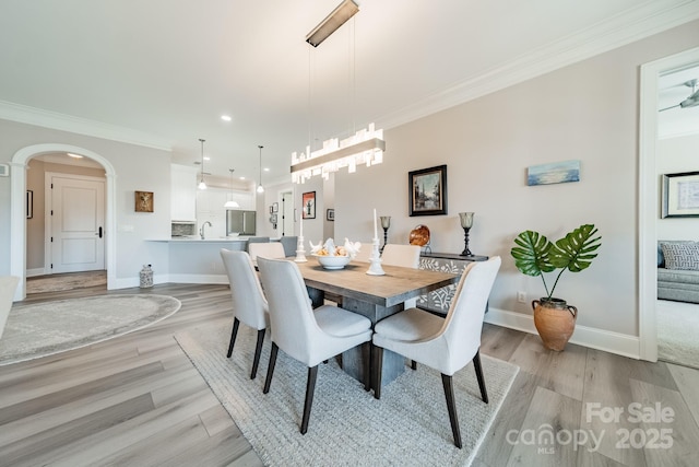 dining area featuring baseboards, arched walkways, light wood-style flooring, and crown molding