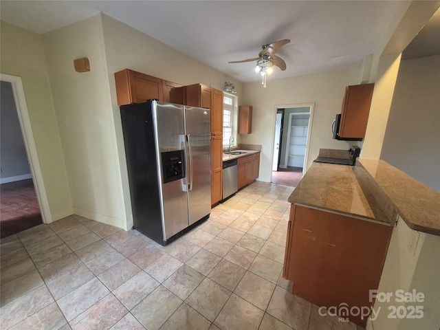 kitchen featuring baseboards, brown cabinetry, ceiling fan, stainless steel appliances, and a sink