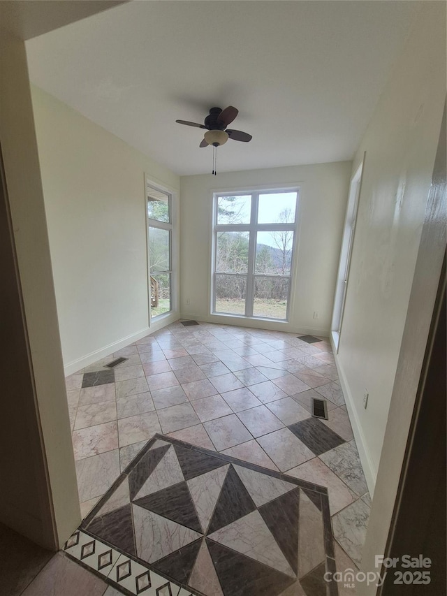 spare room with a ceiling fan, visible vents, and baseboards