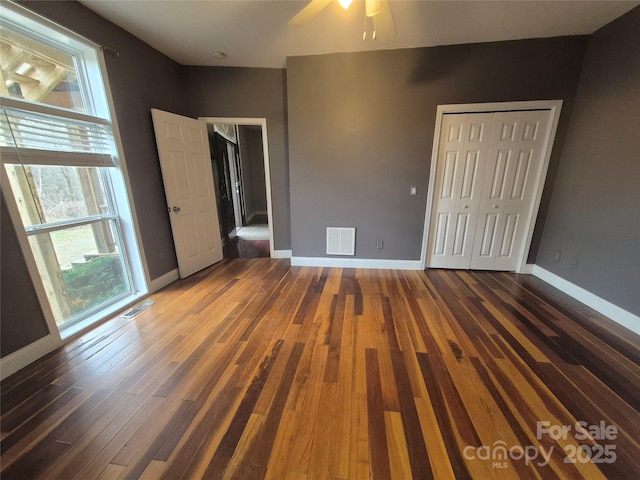 unfurnished bedroom with baseboards, a closet, visible vents, and wood finished floors