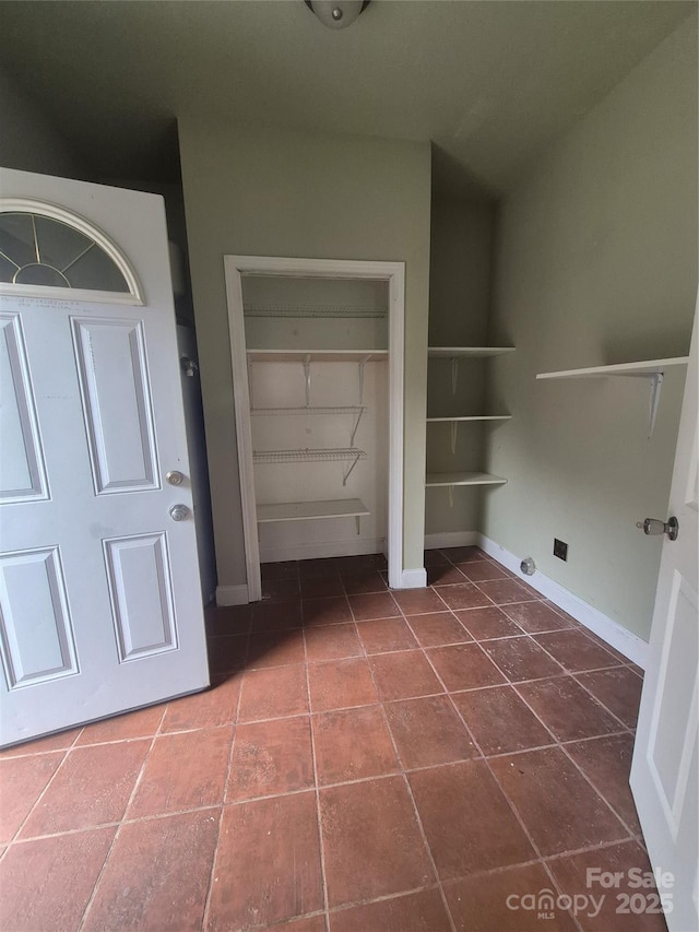 laundry area with built in shelves, dark tile patterned flooring, and baseboards