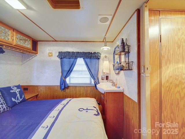 bedroom with a wainscoted wall, visible vents, a sink, and wood walls