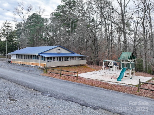 view of front of home with metal roof, playground community, and driveway